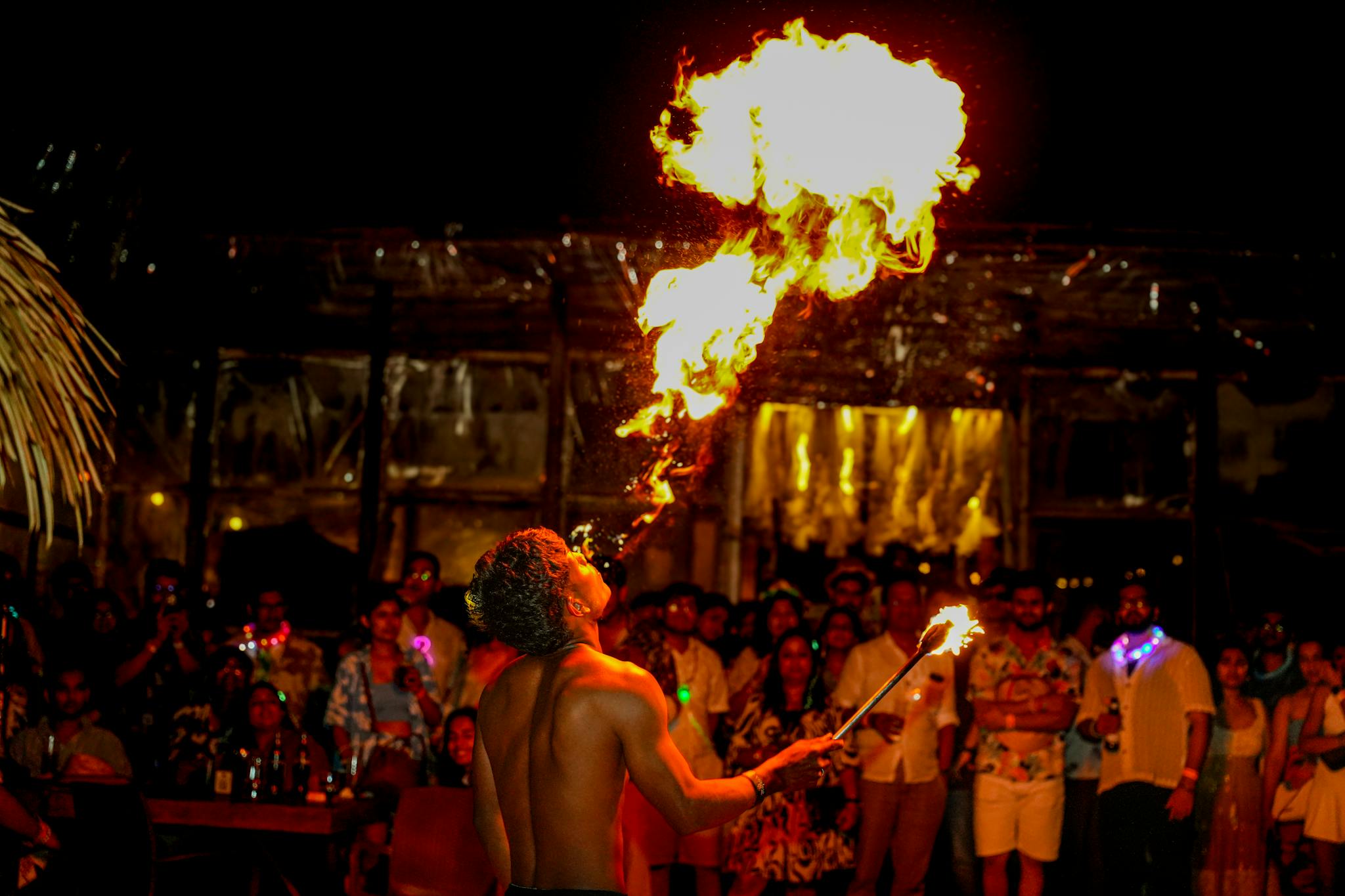 A fire performer mesmerizes a vibrant crowd at an outdoor night party.