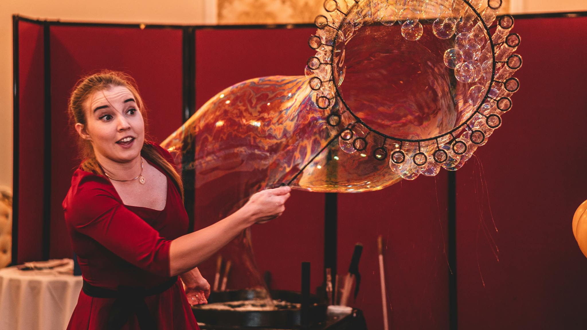 A woman skillfully creates large bubbles at an indoor entertainment event, showcasing bubble art.