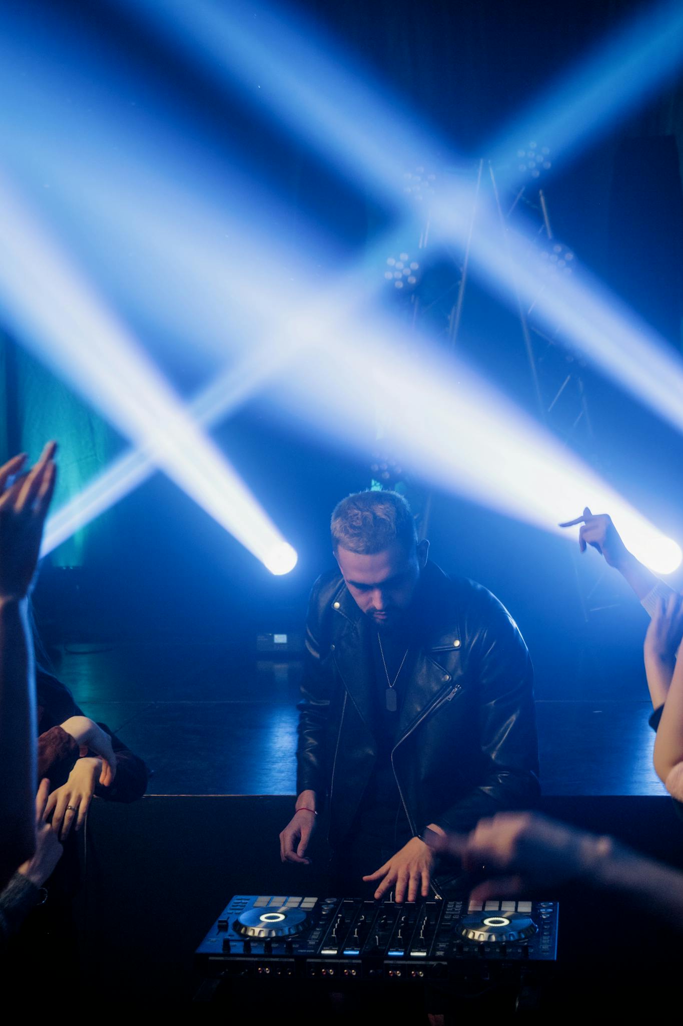 DJ in leather jacket mixes music on stage with vivid disco lights and engaged crowd.